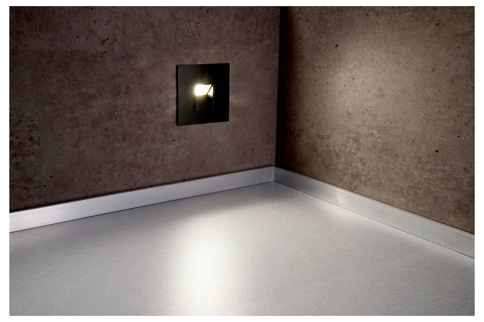 Lege hoekkamer met een kleine wandlamp die de vloer verlicht vanuit een ingebouwde vierkante opening.