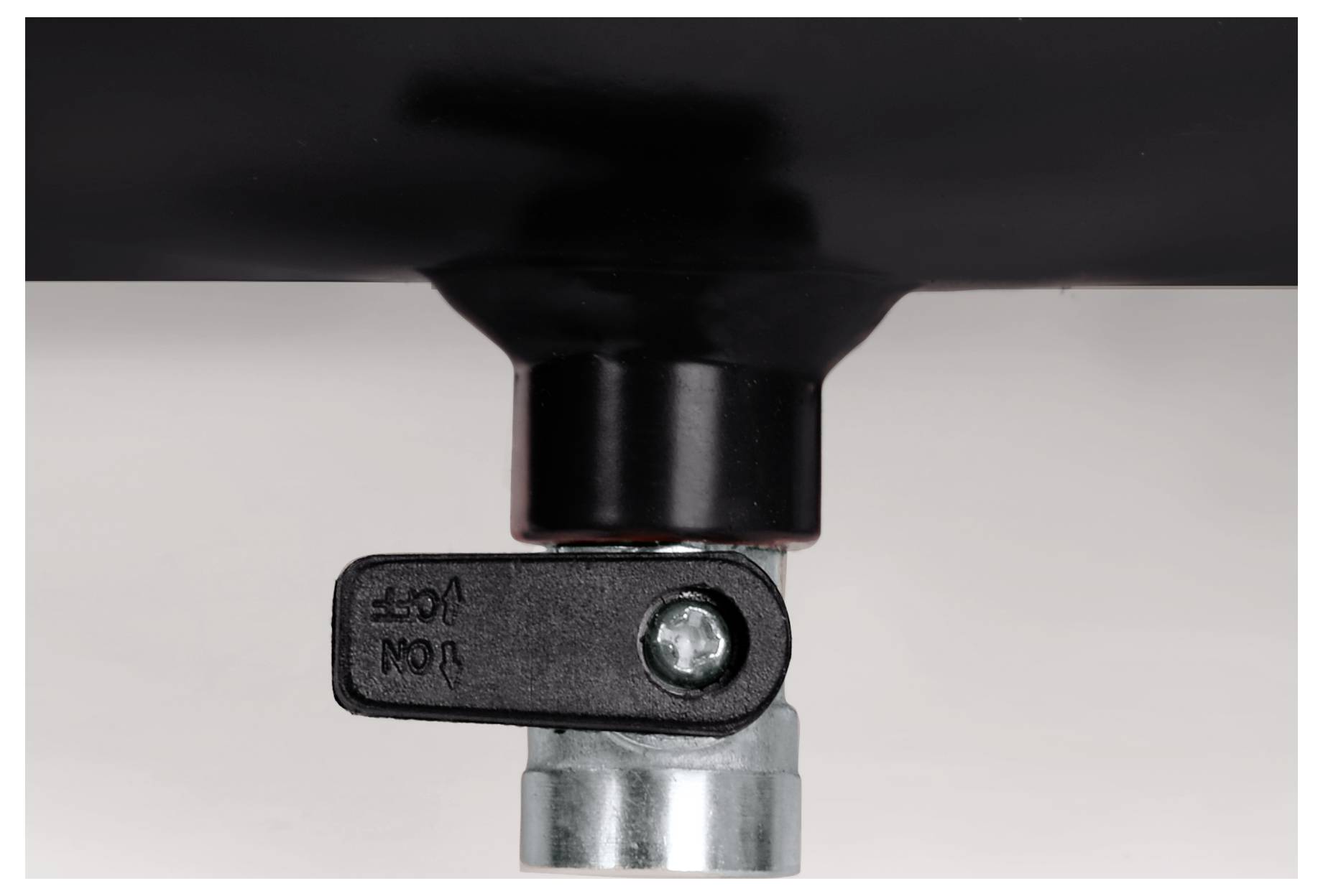 Close-up van een zwart plastic hefboomventiel bevestigd aan een metalen pijp of fitting tegen een eenvoudige achtergrond.