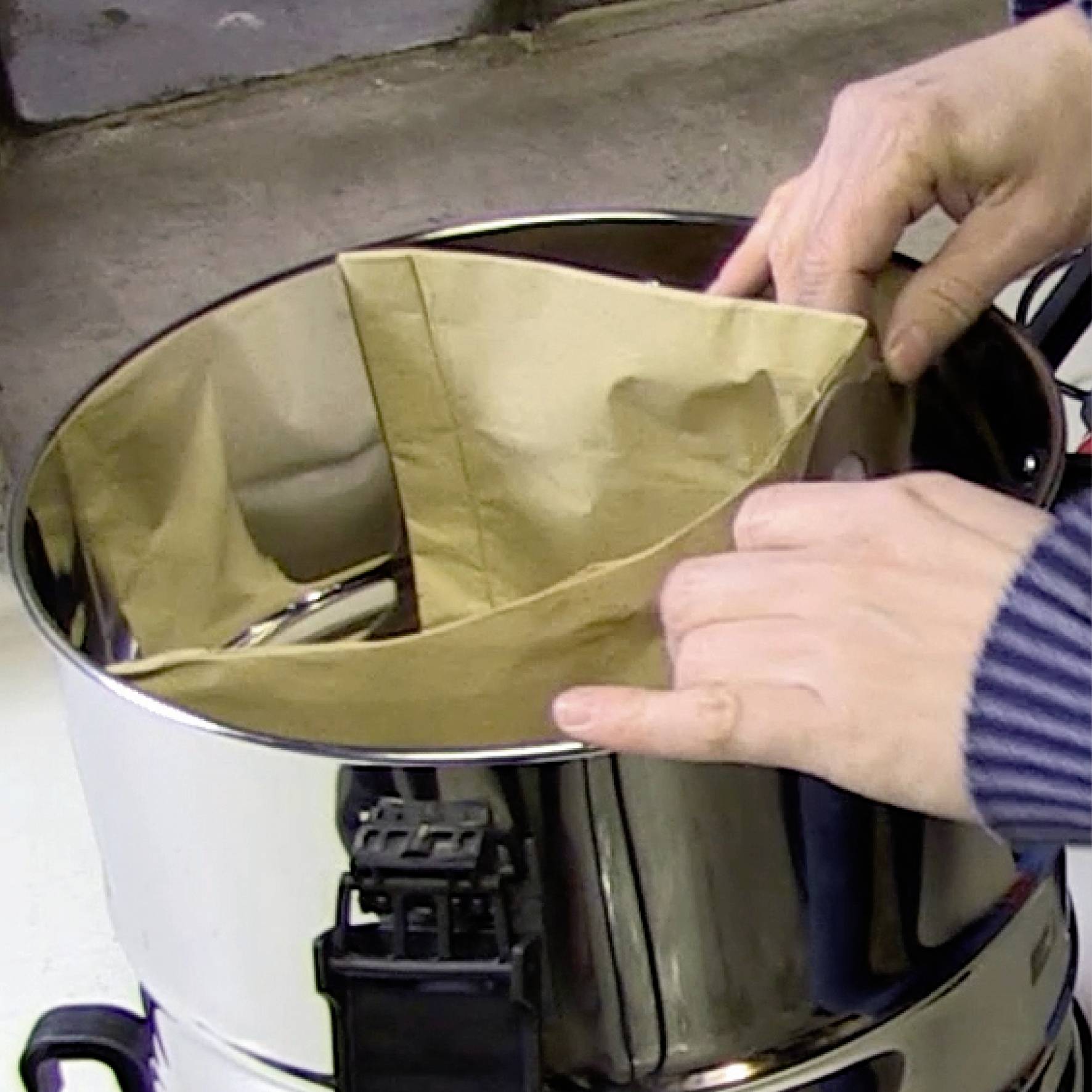 Iemand plaatst een bruine papieren filter in een glanzende koffiemachine.