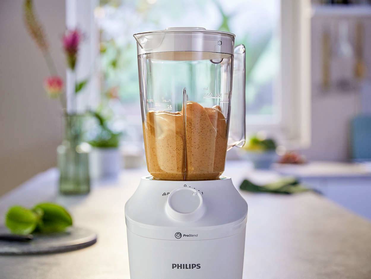 Een staande blender op een aanrecht, gevuld met een oranje smoothie. Op de achtergrond zijn onscherpe keukengerei zichtbaar.