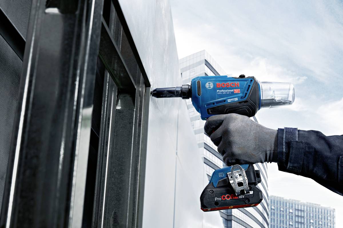 Een persoon gebruikt een Bosch accuschroefmachine op een metalen oppervlak met een stedelijke achtergrond.