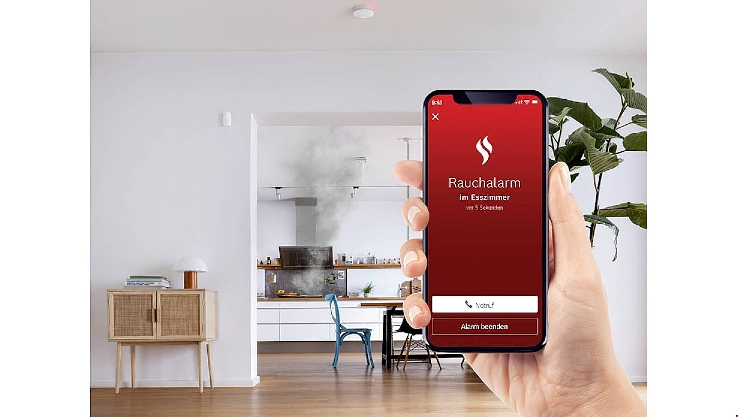 Een hand houdt een smartphone vast die een rookmelder in de eetkamer weergeeft. Op de achtergrond is een keuken met rook zichtbaar.