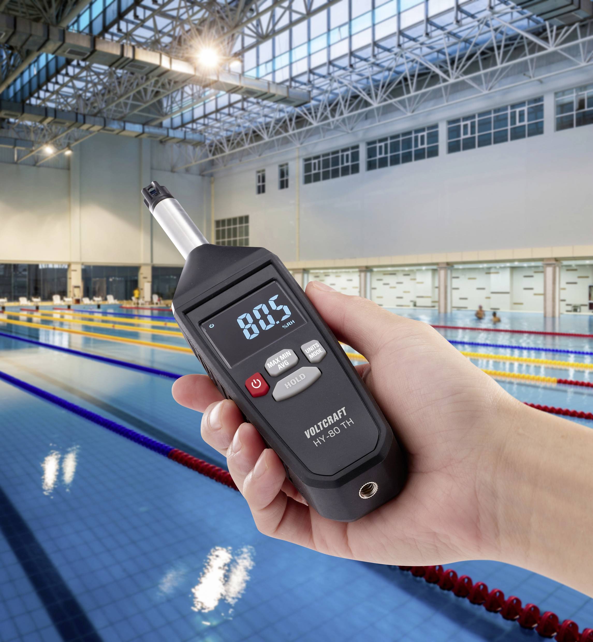 Een handapparaat toont een waarde van 80,5 boven een zwembad. Het apparaat meet mogelijk water- of ruimteparameters.