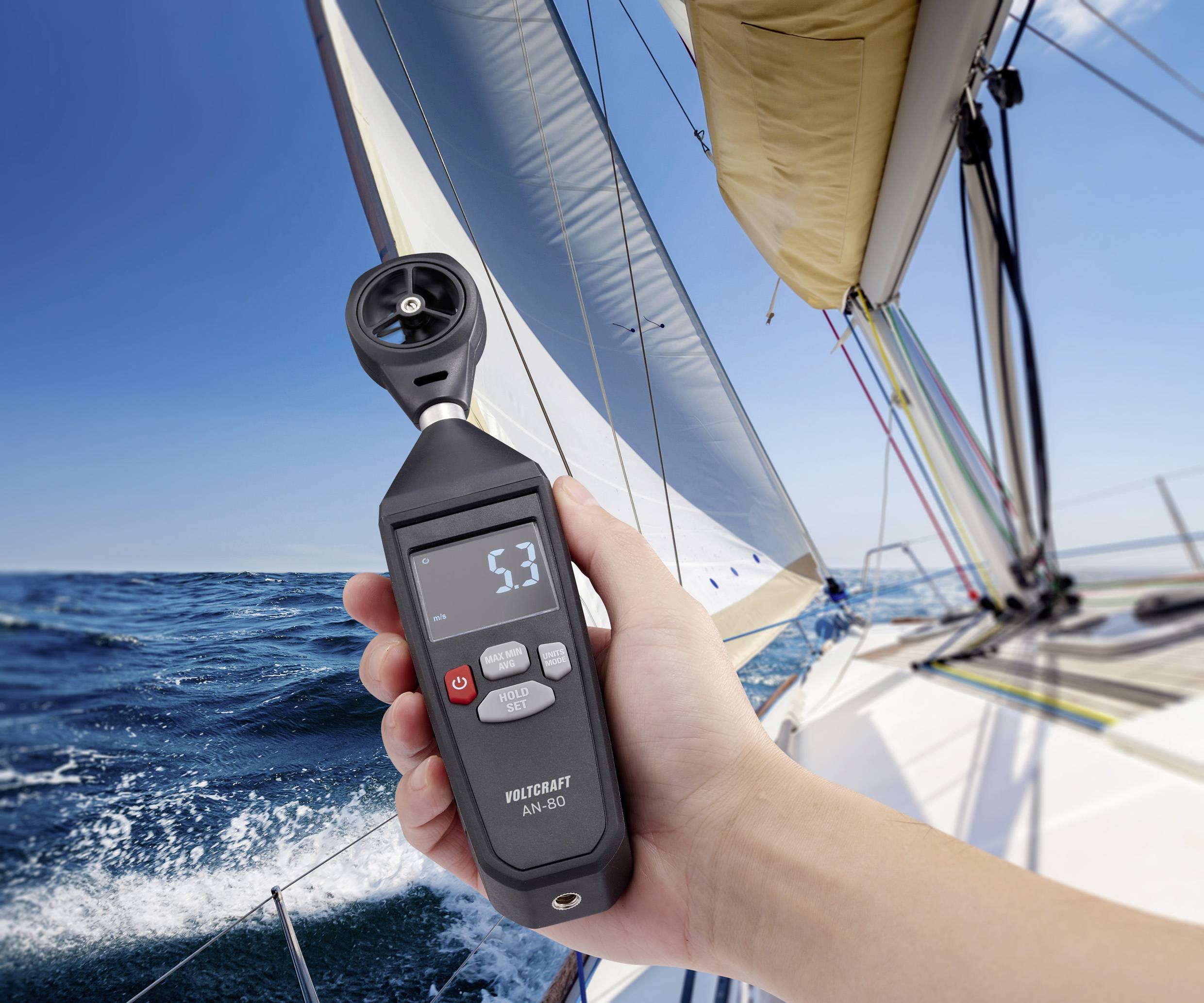 Een persoon houdt een anemometer vast die een windsnelheid van 5,3 aangeeft, op een zeilboot bij zonnig weer op zee.