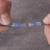 Twee handen houden een blauw kabel vast met een transparente, blauwe krimpverbinding; merkenlogo 'QUADRIOS'.