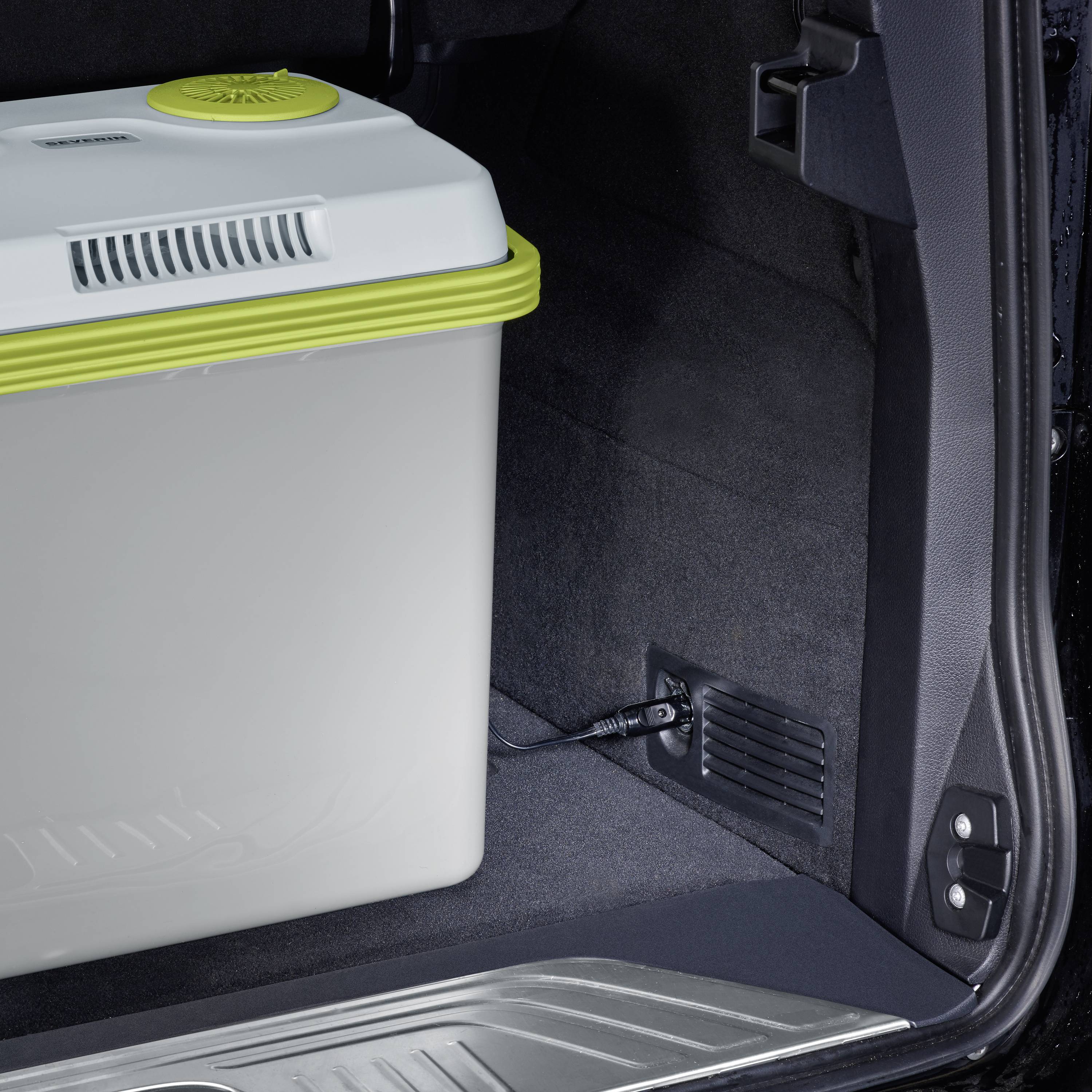 Koelbox in de kofferbak van een auto, geopend met zichtbare binnenkant. De box is wit met een groene rand.