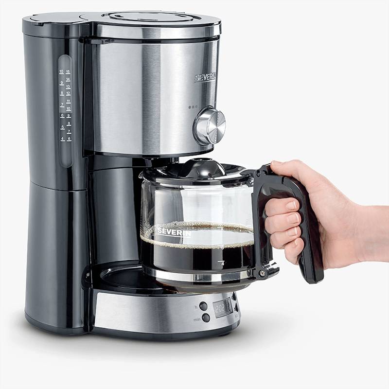 Een hand houdt de glazen kan van een zwarte koffiemachine vast, gevuld met verse koffie. De machine heeft een modern design.