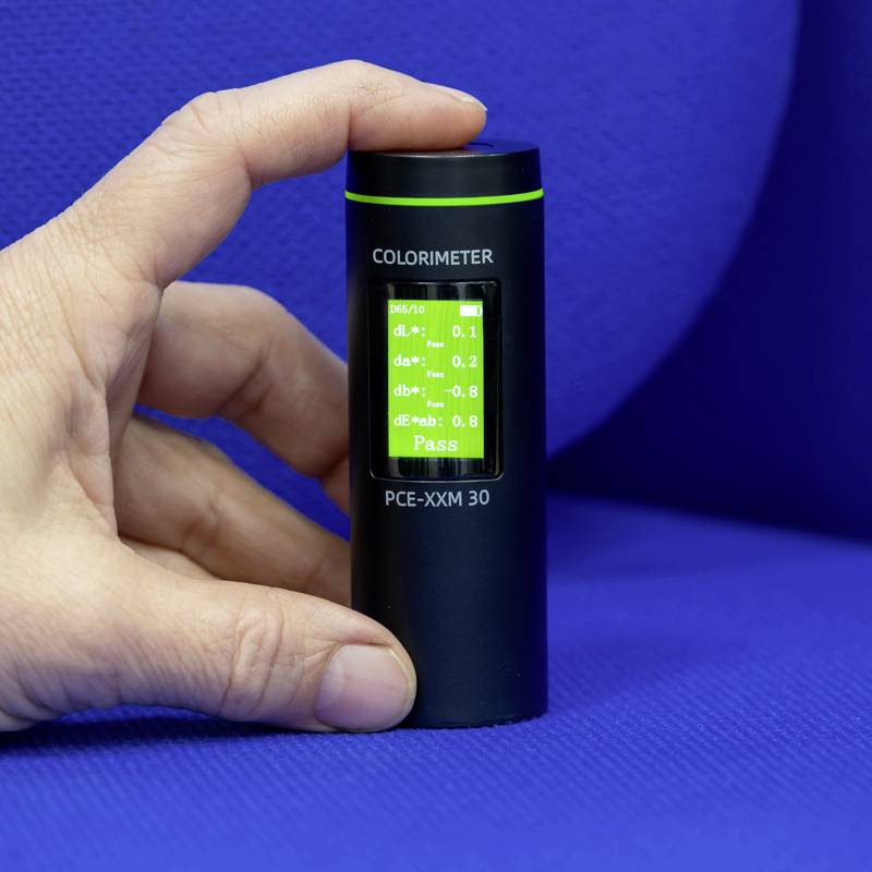 Een hand houdt een draagbaar colorimeter vast met een groen verlicht display dat meetwaarden weergeeft. Het apparaat wordt gebruikt voor kleuranalyse.