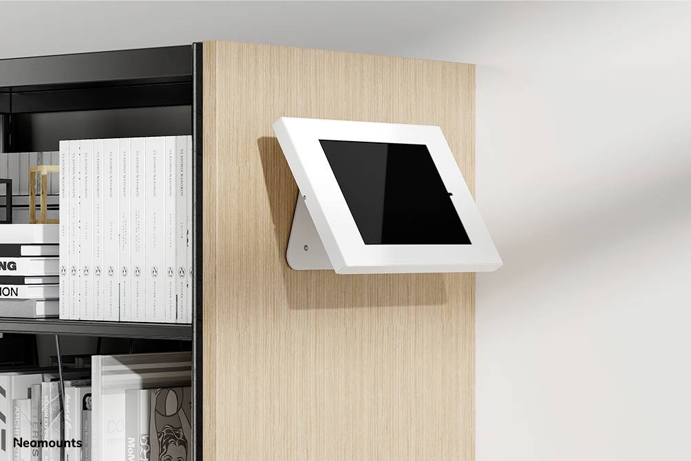 Tablet in een witte houder gemonteerd aan een houten muur naast een boekenkast. De houder is draaibaar.