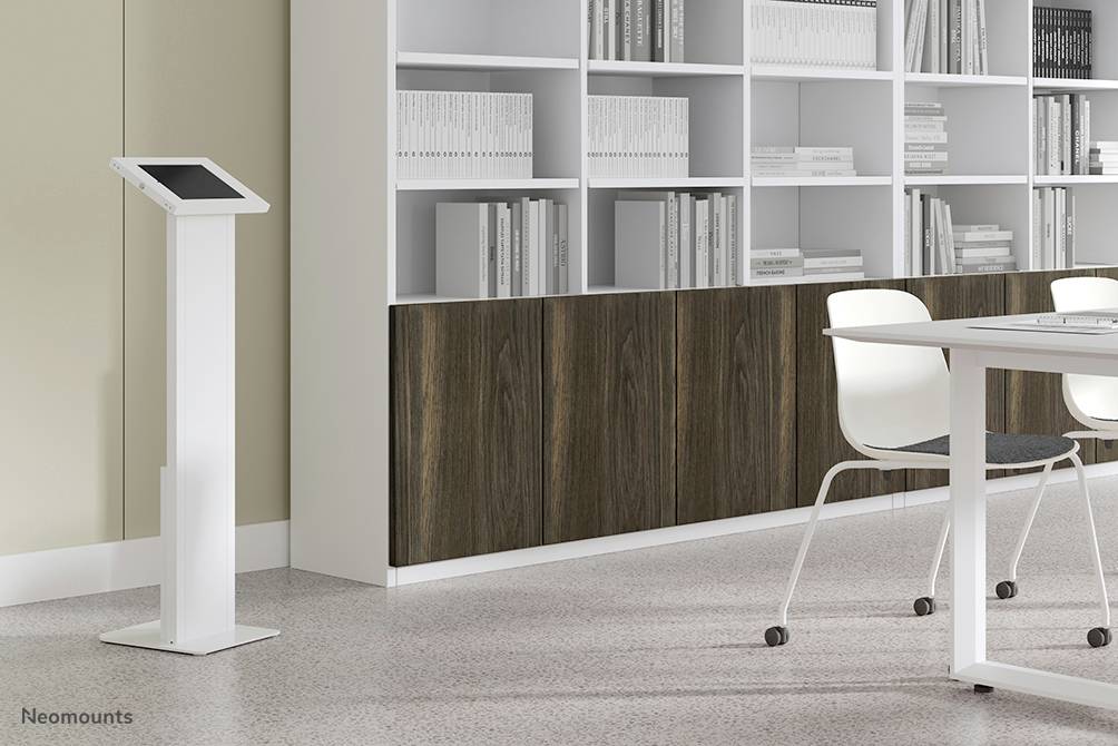 Een modern kantoor met een tablet op een standaard, witte stoelen, een tafel en boekenplanken op de achtergrond.