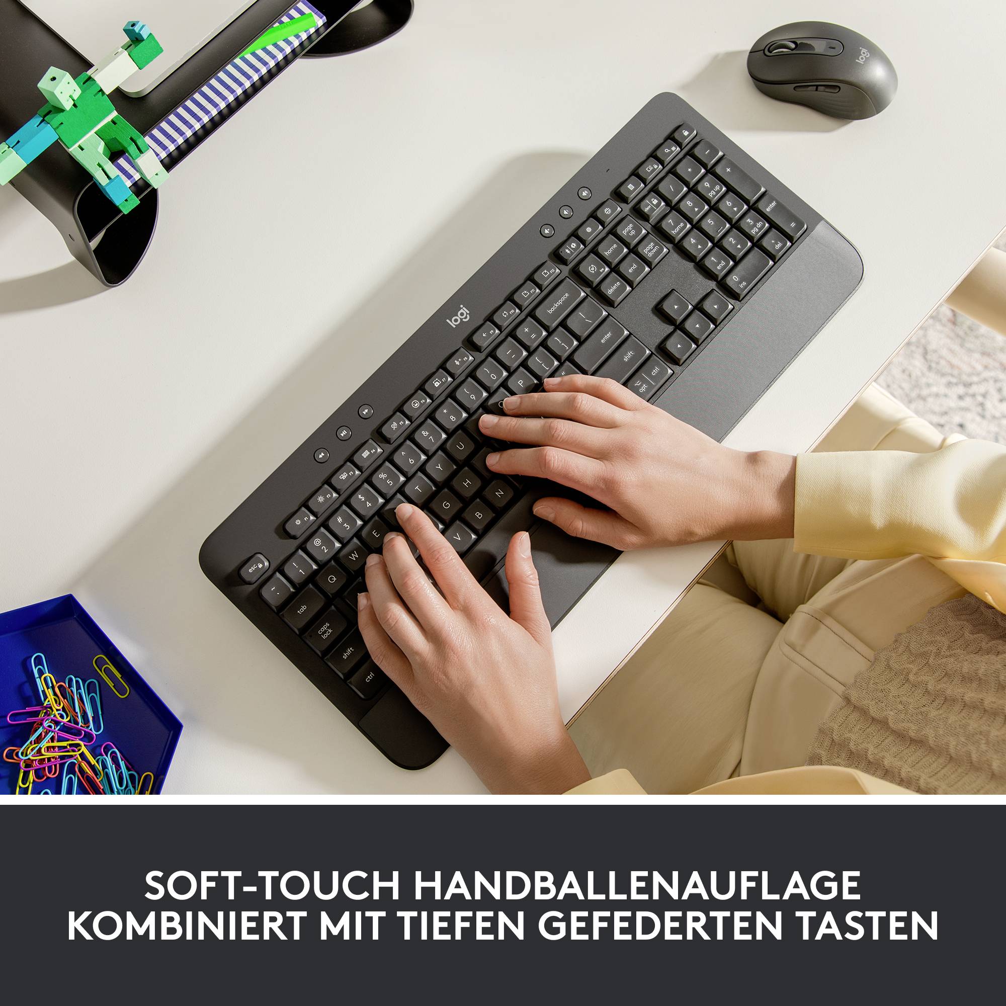 Een persoon typt op een zwart toetsenbord met een soft-touch polssteun. Tekst in de afbeelding: 'Soft-touch polssteun gecombineerd met diep veerende toetsen'.
