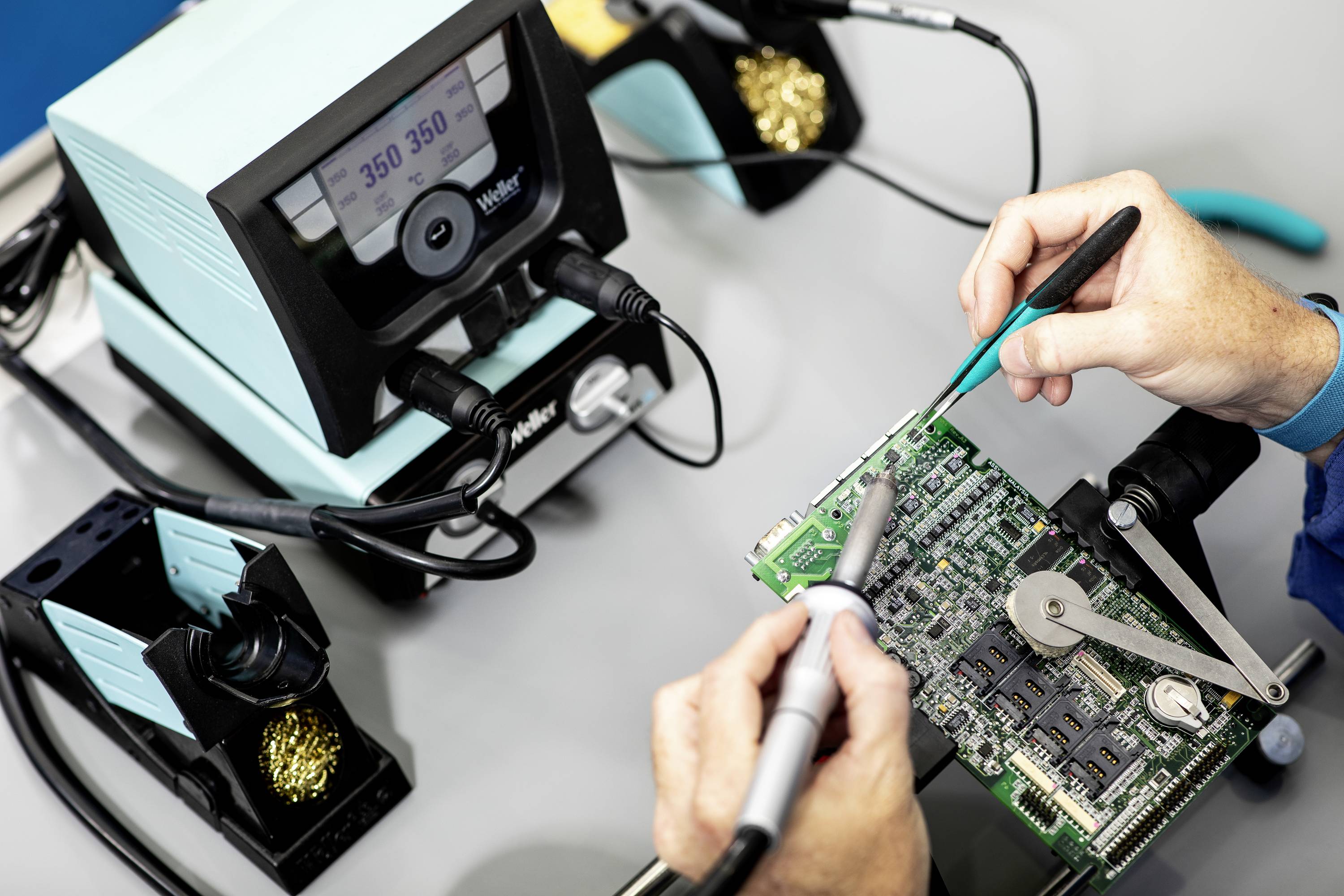 Een persoon repareert een printplaat met een soldeerbout, pincet en digitale soldeerbout. Close-up van het technische proces.