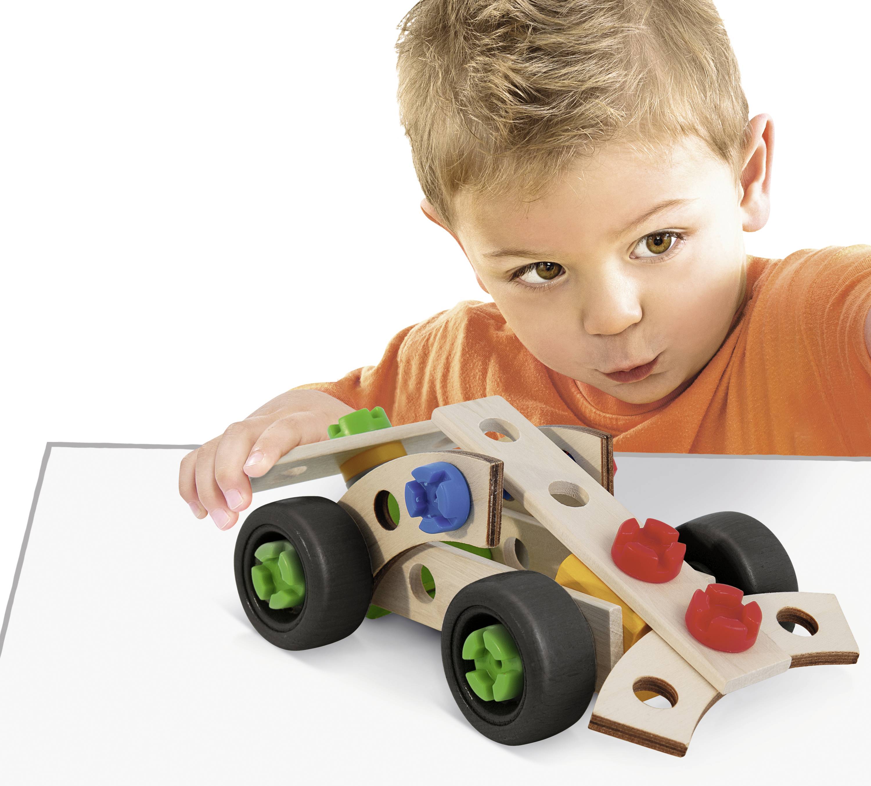 Een kind in een oranje shirt speelt geconcentreerd met een kleurrijke speelgoedauto op een witte tafel.