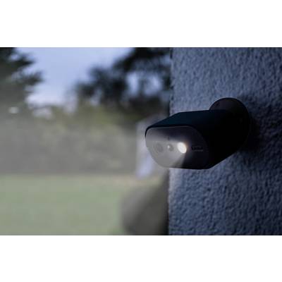 Buitencamera met nachtzicht en bewegingssensor, bevestigd aan een muur, in een tuin met een onscherpe achtergrond.