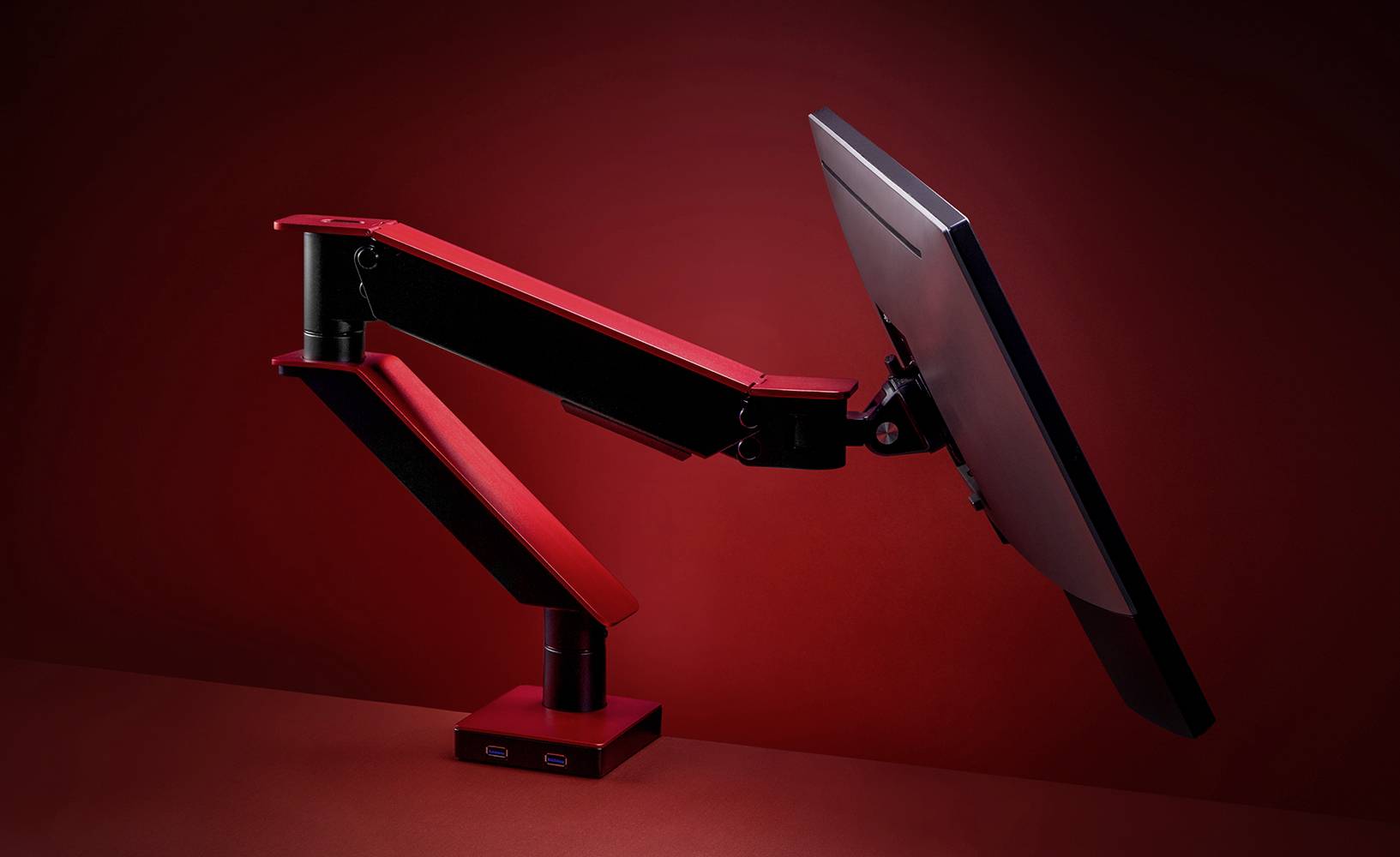 Een ergonomische monitorarm in het rood, houdt een scherm in een zwevende positie voor een rode achtergrond.