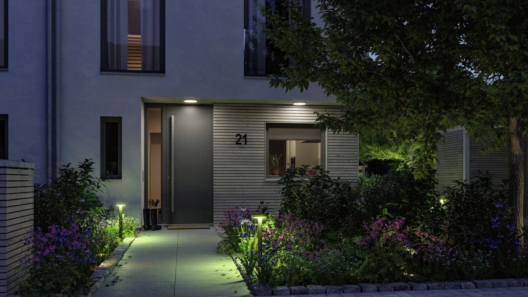 Entree van een modern huis 's nachts, verlicht door padverlichting, omgeven door een keurig onderhouden tuin met bloeiende planten.