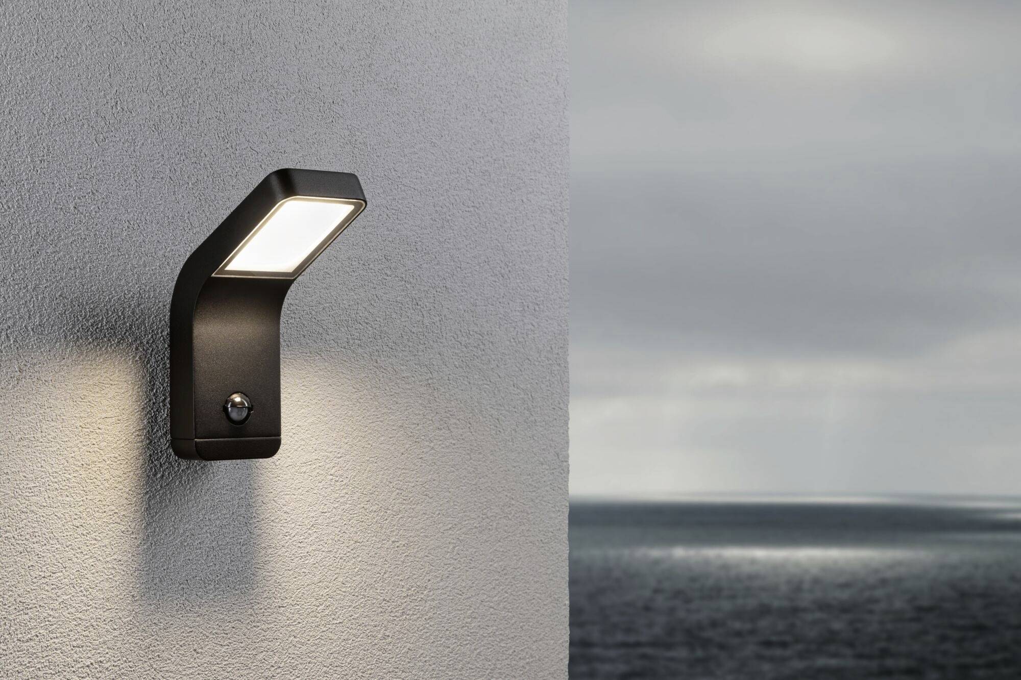 Buitenwandlamp aan een muur, schijnt bij bewolkte hemel met uitzicht op zee.