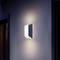 Een moderne wandlamp met zacht, wit licht, bevestigd aan een grijze muur. Hij verlicht de ruimte subtiel en gelijkmatig.