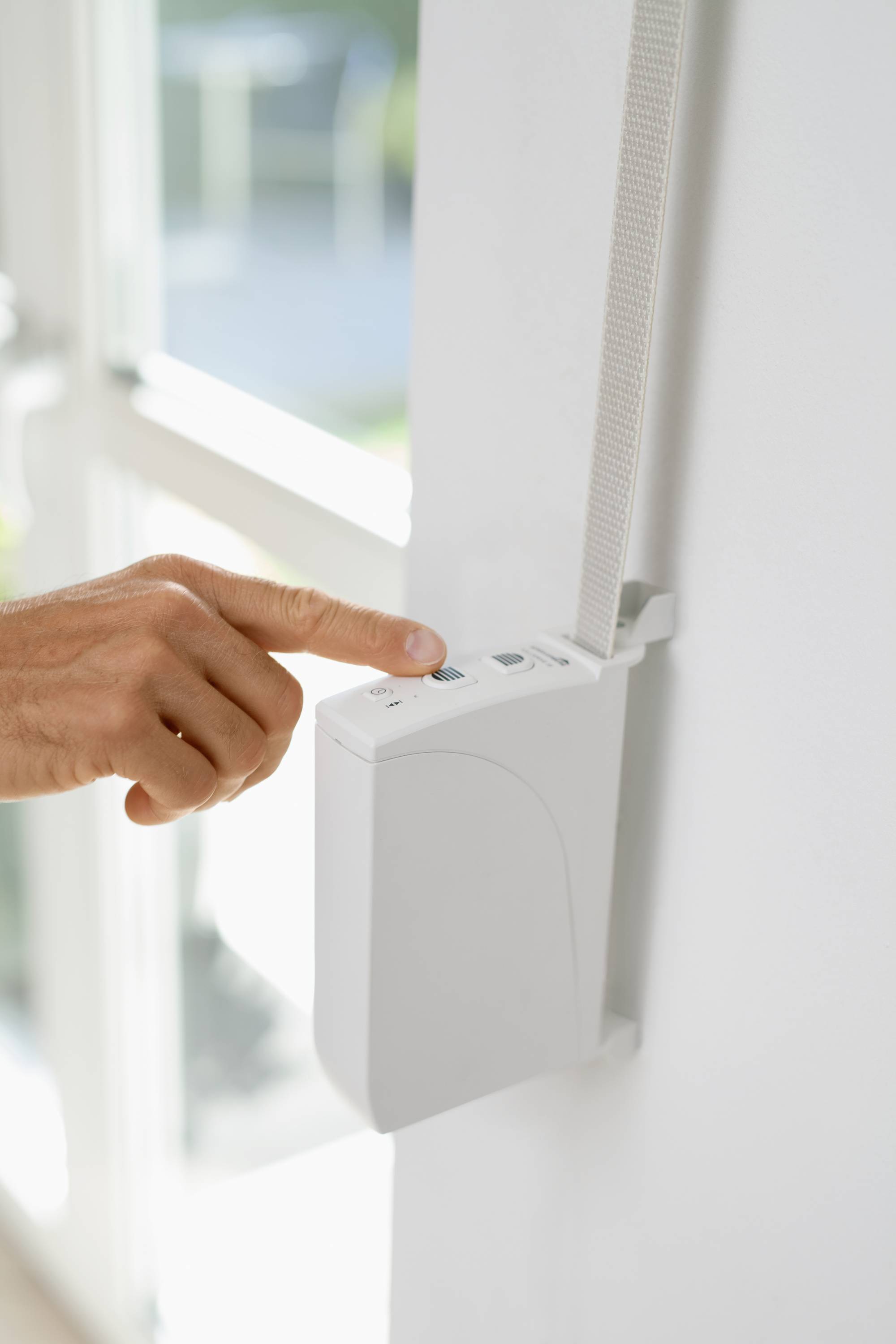 'Een hand drukt op een knop van een jaloeziebesturing aan de muur.'