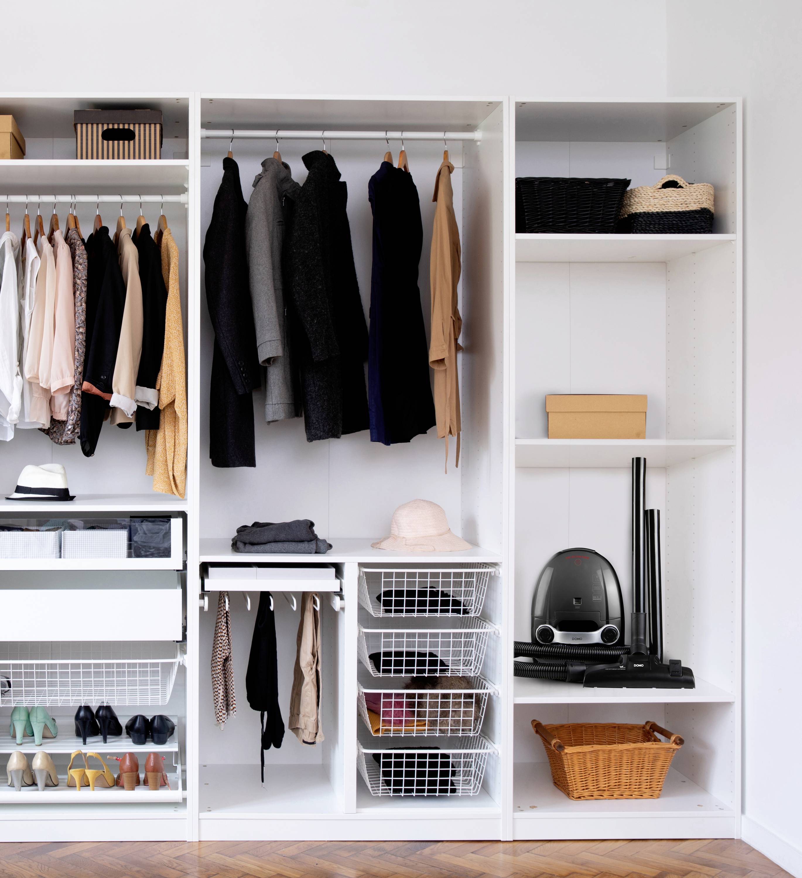 Kledingkast met hangrekken, laden en vakken, gevuld met kleding, schoenen, hoeden en een stofzuiger rechts.