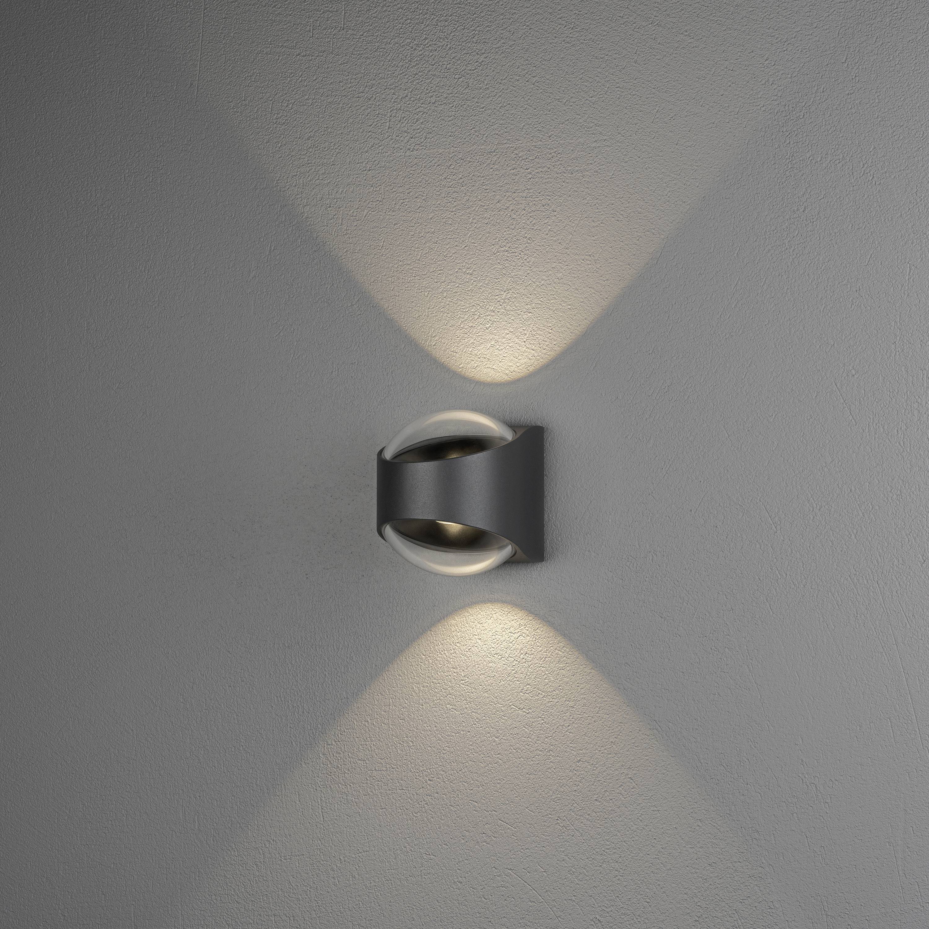 Wandlamp aan een grijze muur die zowel naar boven als naar beneden schijnt en zacht licht creëert in een decoratief patroon.