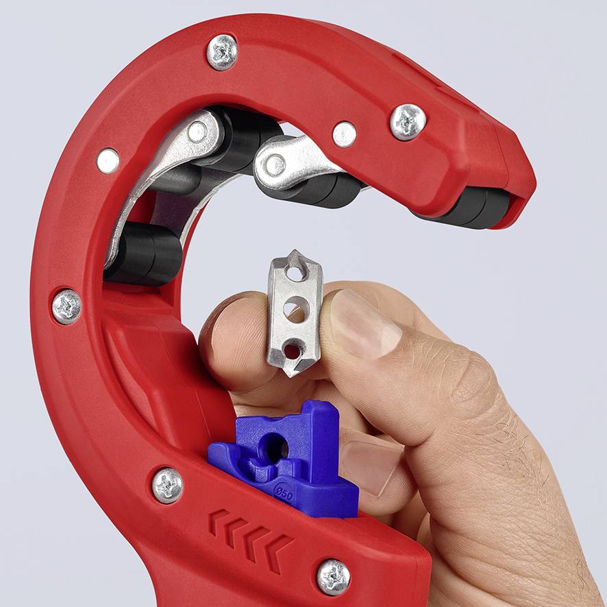 Een hand houdt een klein metalen onderdeel vast voor een rode buizensnijder die wordt gebruikt voor het doorknippen van buizen.