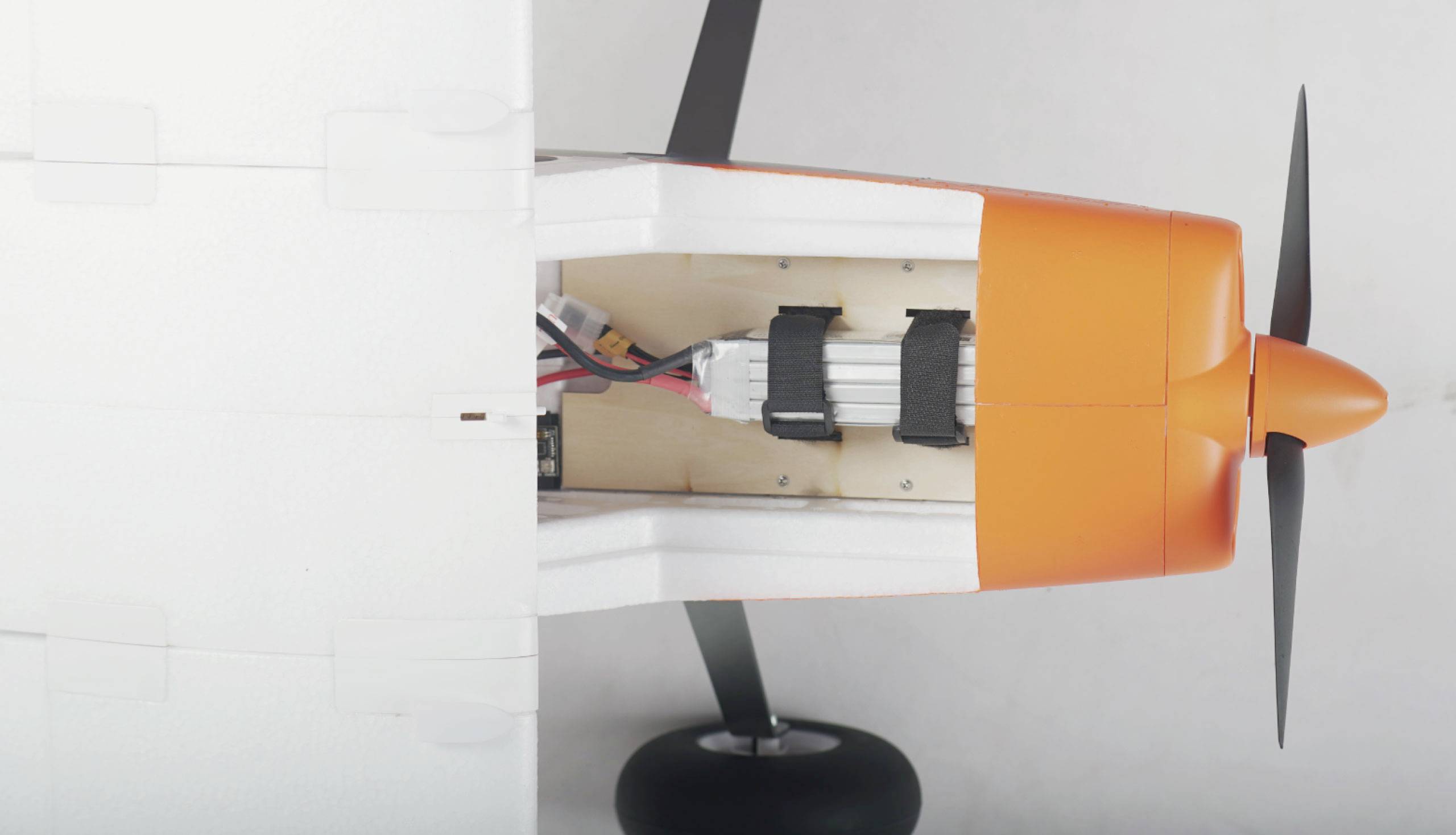 Modelvliegtuig vanuit een bovenaanzicht, toont de elektronica binnenin de oranje en witte romp, met propeller en landingsgestel.