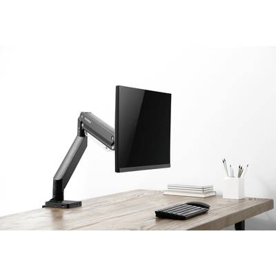 Een computermonitor is bevestigd aan een flexibele steunarm boven een bureau. Op de tafel liggen notitieboeken en pennen.