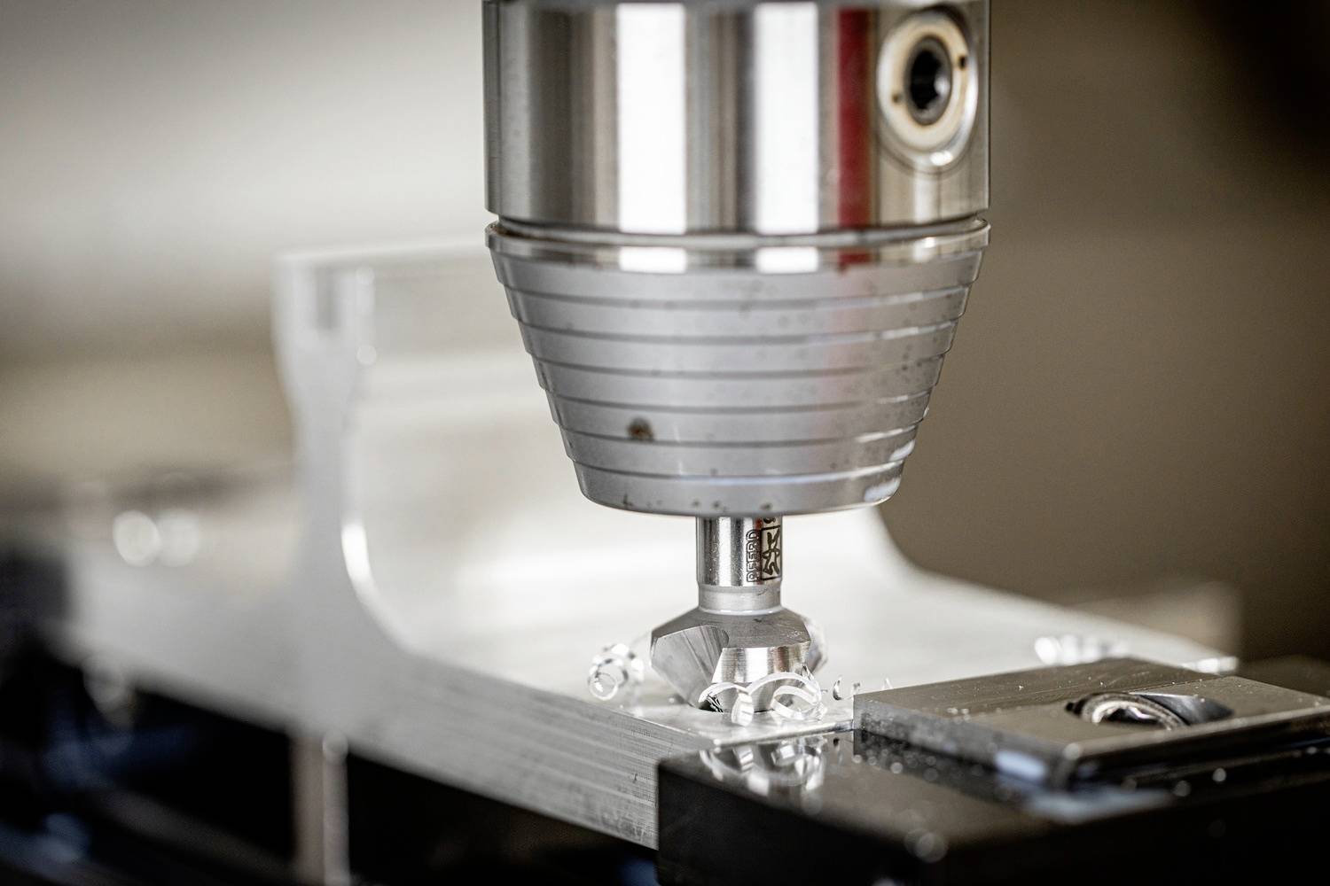 Een CNC-machine freest nauwkeurig een metalen onderdeel. De boor beweegt zich verticaal om gedetailleerde sneden op het zilveren oppervlak te maken.