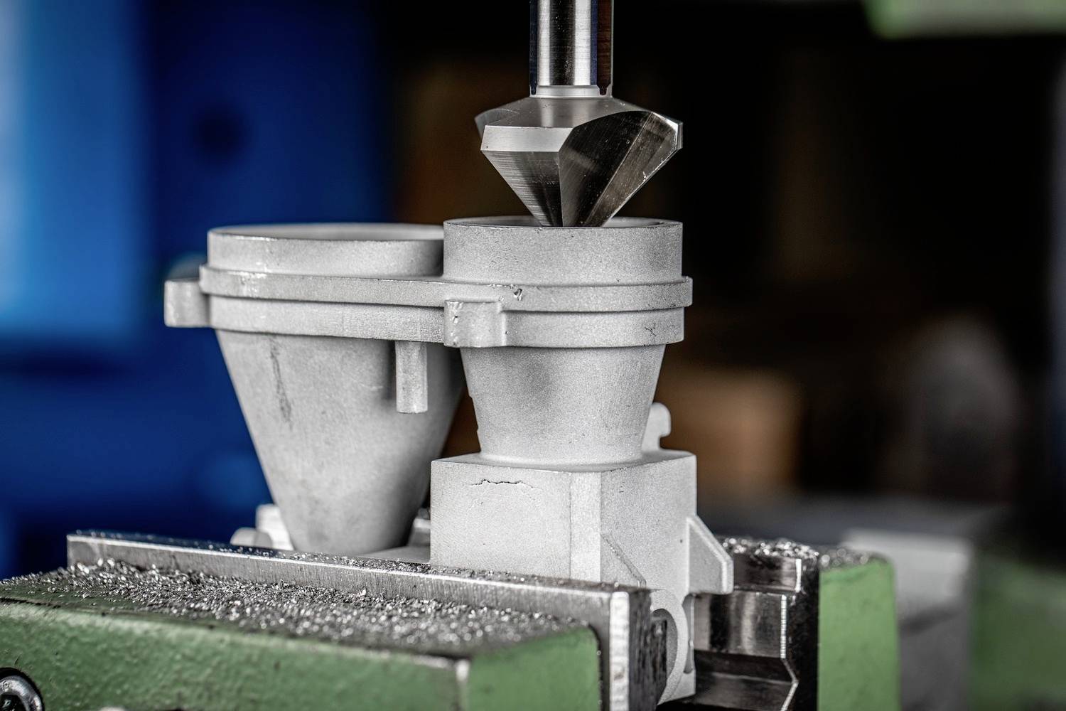 Een metalen boormachine bewerkt nauwkeurig het oppervlak van een werkstuk. Op de achtergrond is onscherpe werkplaatsapparatuur zichtbaar.