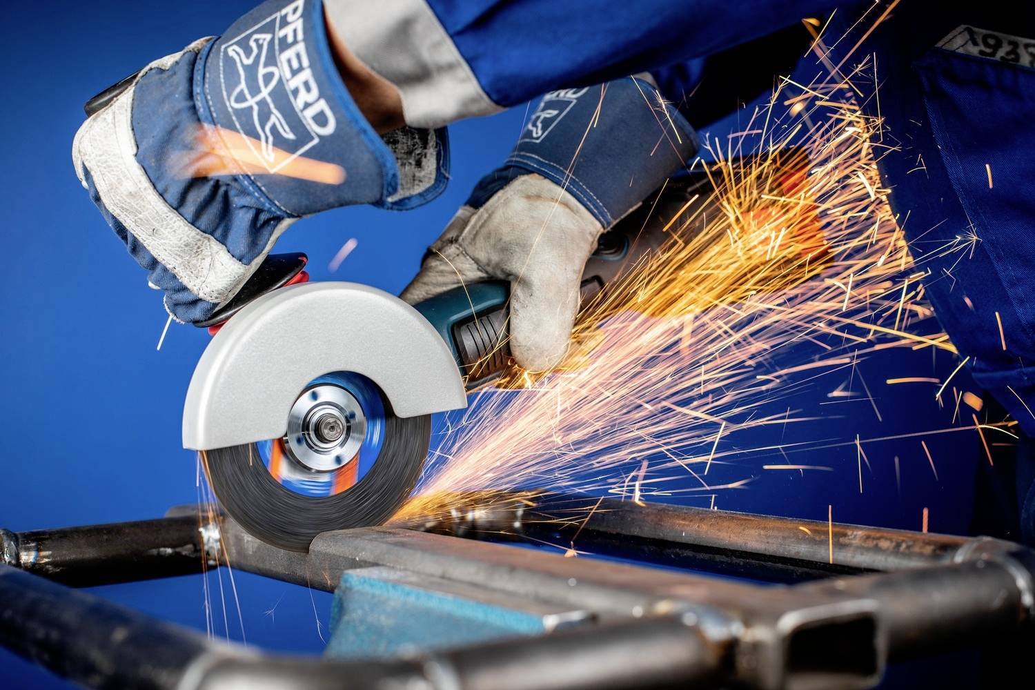 Een persoon in beschermende kleding snijdt een metalen buis met een haakse slijper. Vonken vliegen in alle richtingen.