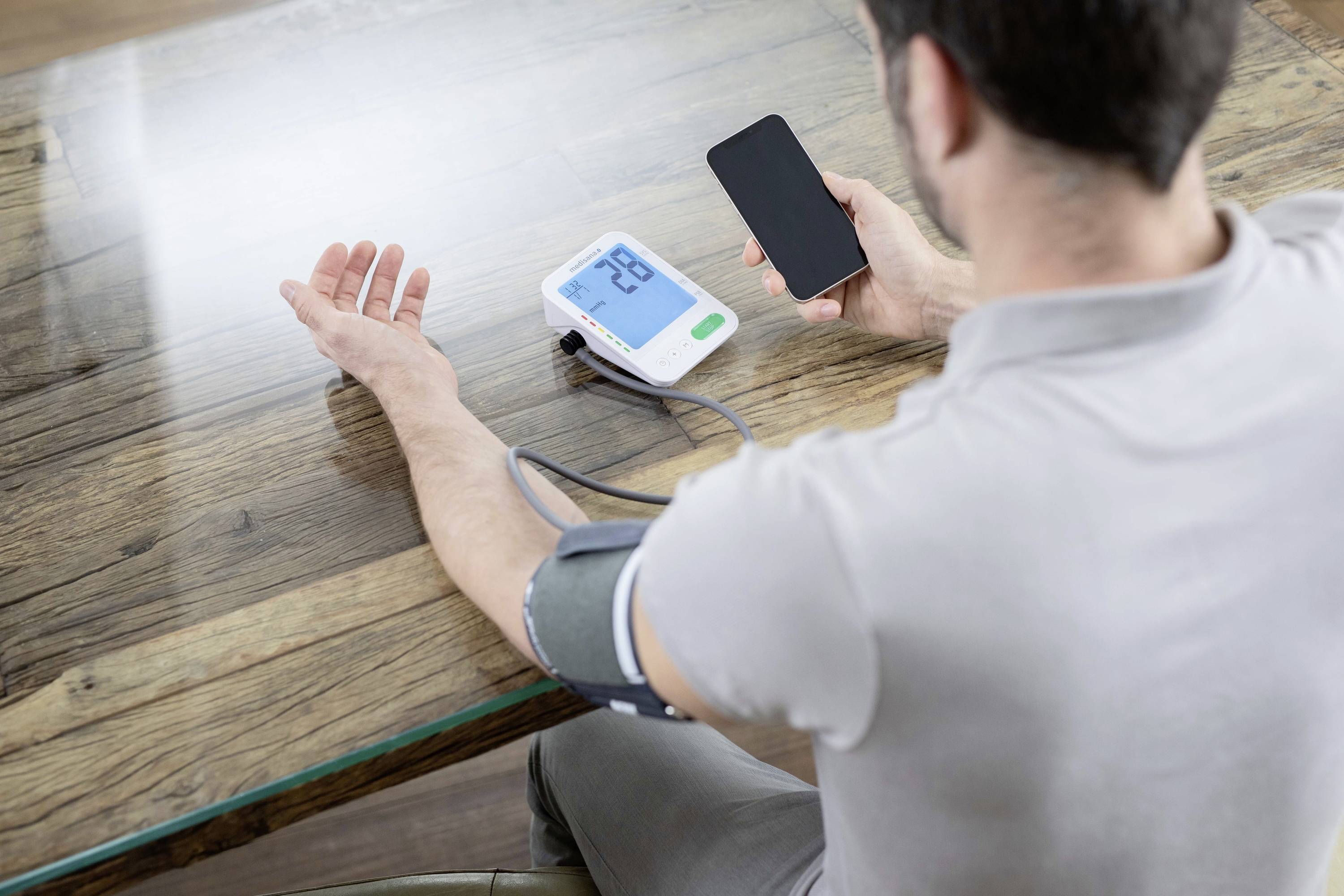 Een persoon meet de bloeddruk met een digitaal apparaat en houdt een smartphone in de andere hand.