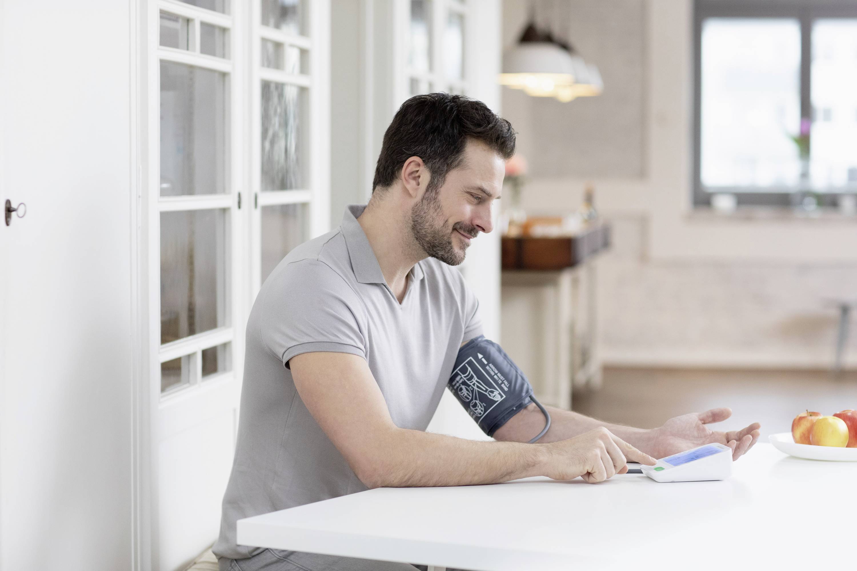 Een man meet zijn bloeddruk thuis met een digitaal bloeddrukmeetapparaat terwijl hij aan tafel zit.