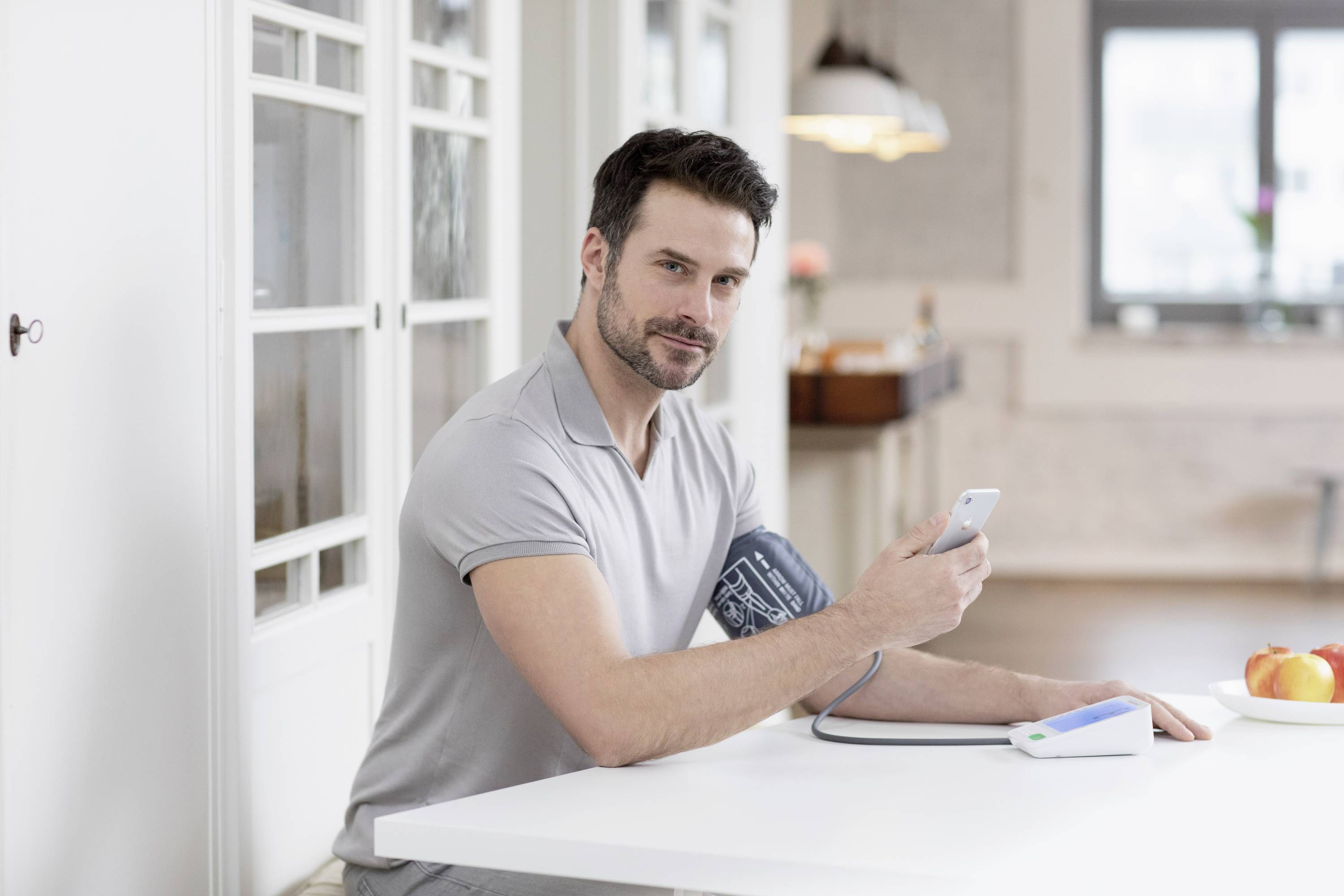 Een man meet zijn bloeddruk met een digitaal meetapparaat en controleert de resultaten op een smartphone.