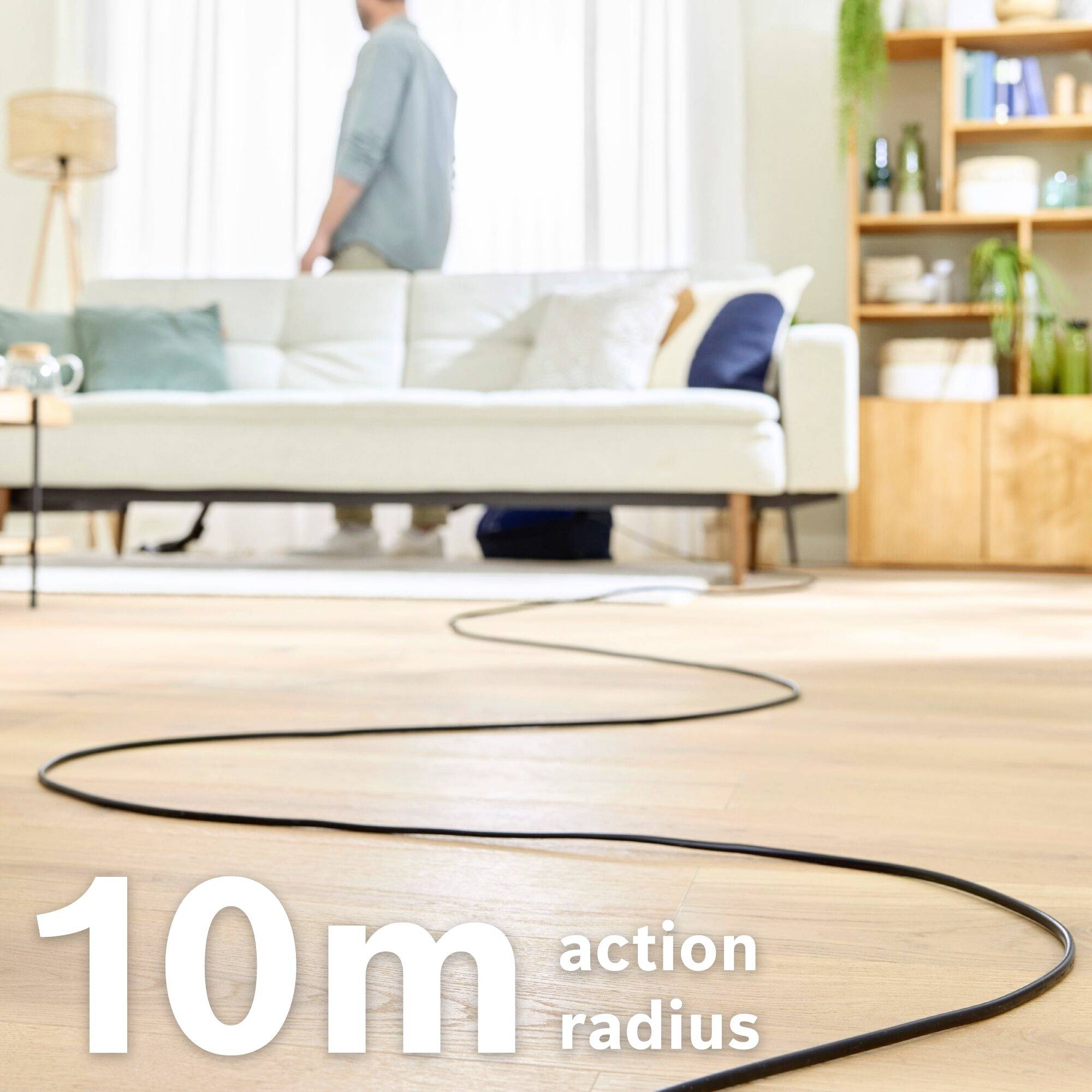 '10 m actieradius' op houten vloer, op de achtergrond bank en man met licht overhemd staand.