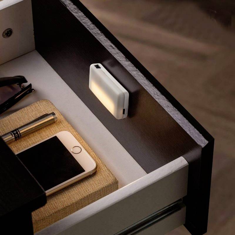 Open lade met een mobiele telefoon naast een notitieboek. Bovenaan de lade is een rechthoekig verlicht licht bevestigd.