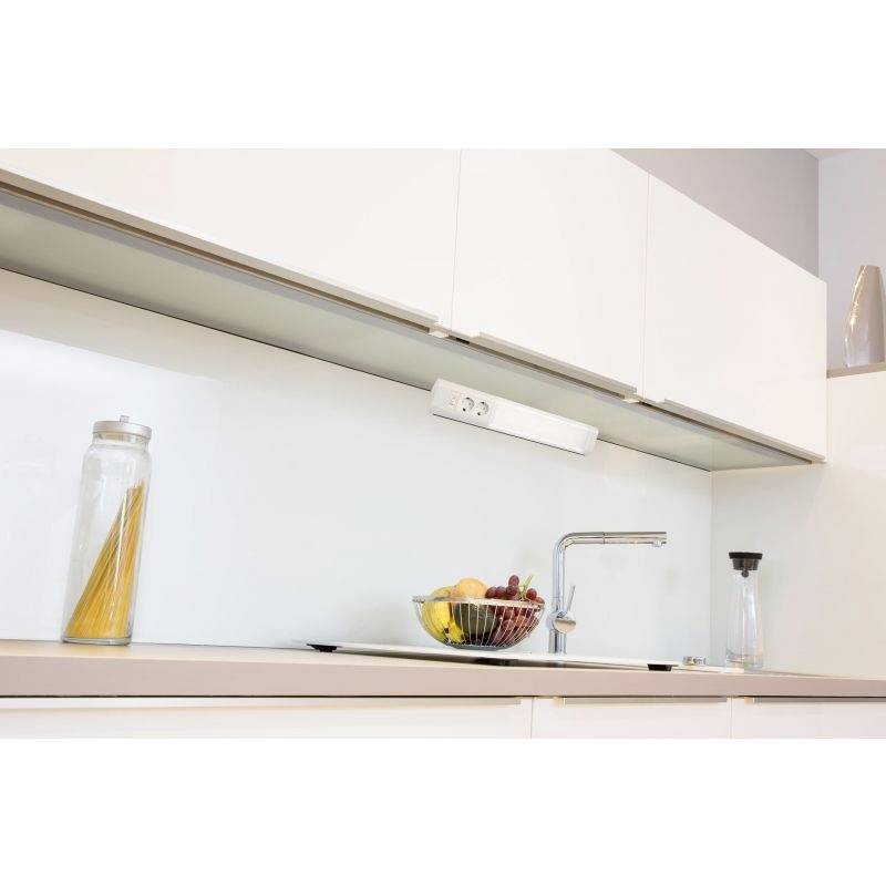 Een moderne keuken met witte kasten, geïntegreerd stopcontact, fruitmotief op het aanrecht, kraan en een vaas met pasta.