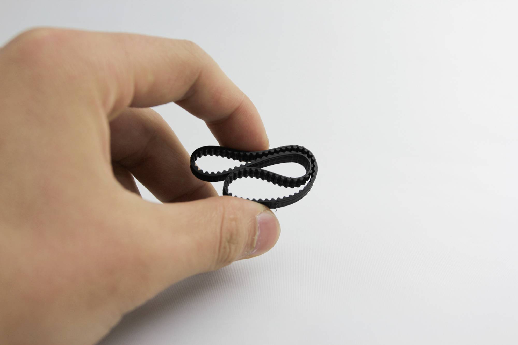 Een hand houdt een kleine zwarte rubberen band vast voor een neutrale achtergrond.