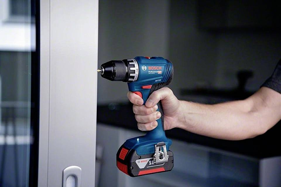 Een hand houdt een blauwe accuschroefboormachine voor een raam.