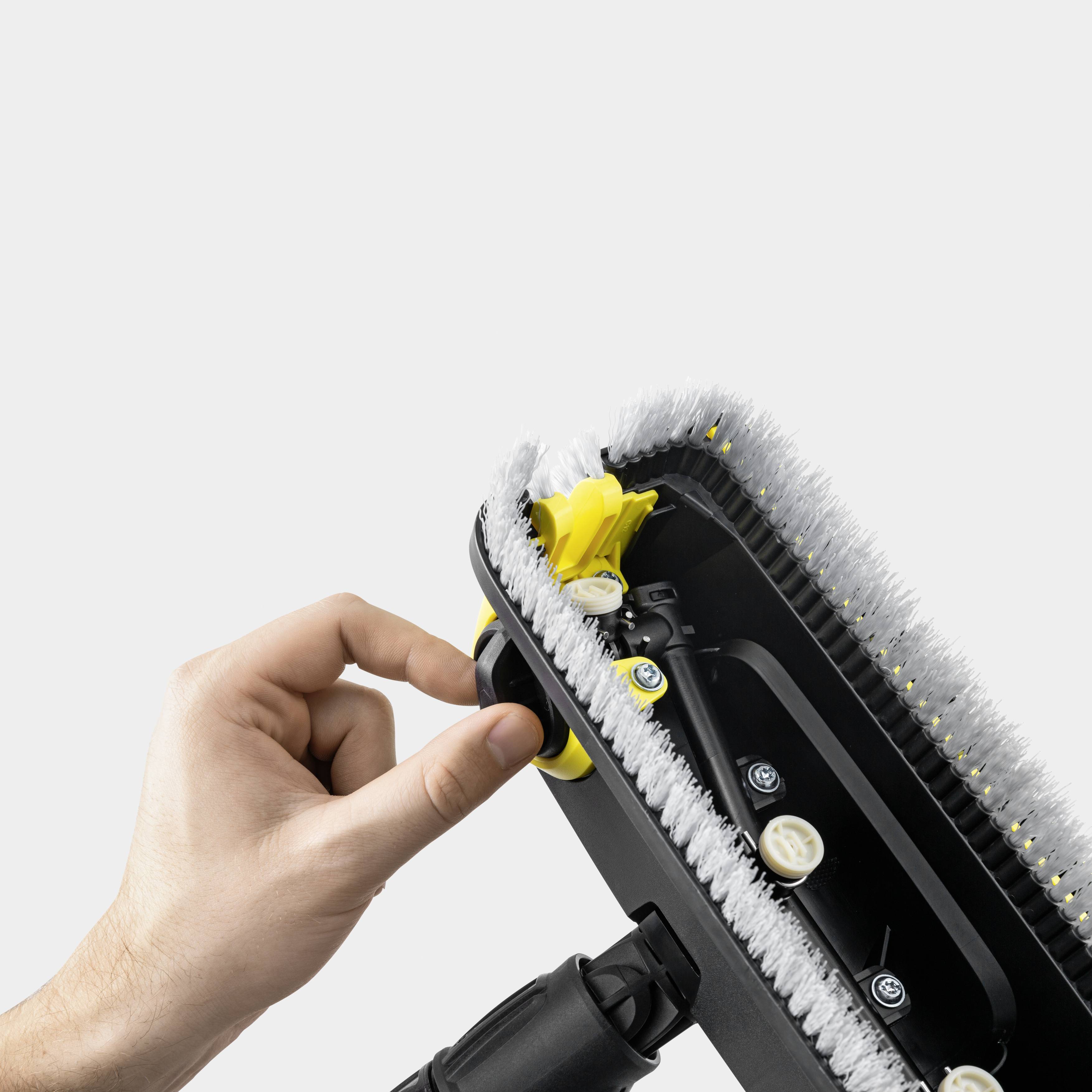 Een hand houdt een vloeronderhoudsapparaat vast met zicht op de onderkant, waarop verschillende roterende borstels en gele tandwielen te zien zijn.