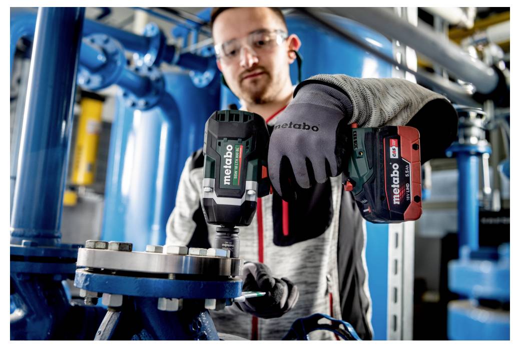 Een persoon die een elektrisch gereedschap gebruikt op industriële machines, terwijl hij beschermende handschoenen en een veiligheidsbril draagt, wat veiligheid en precisiewerk aangeeft.