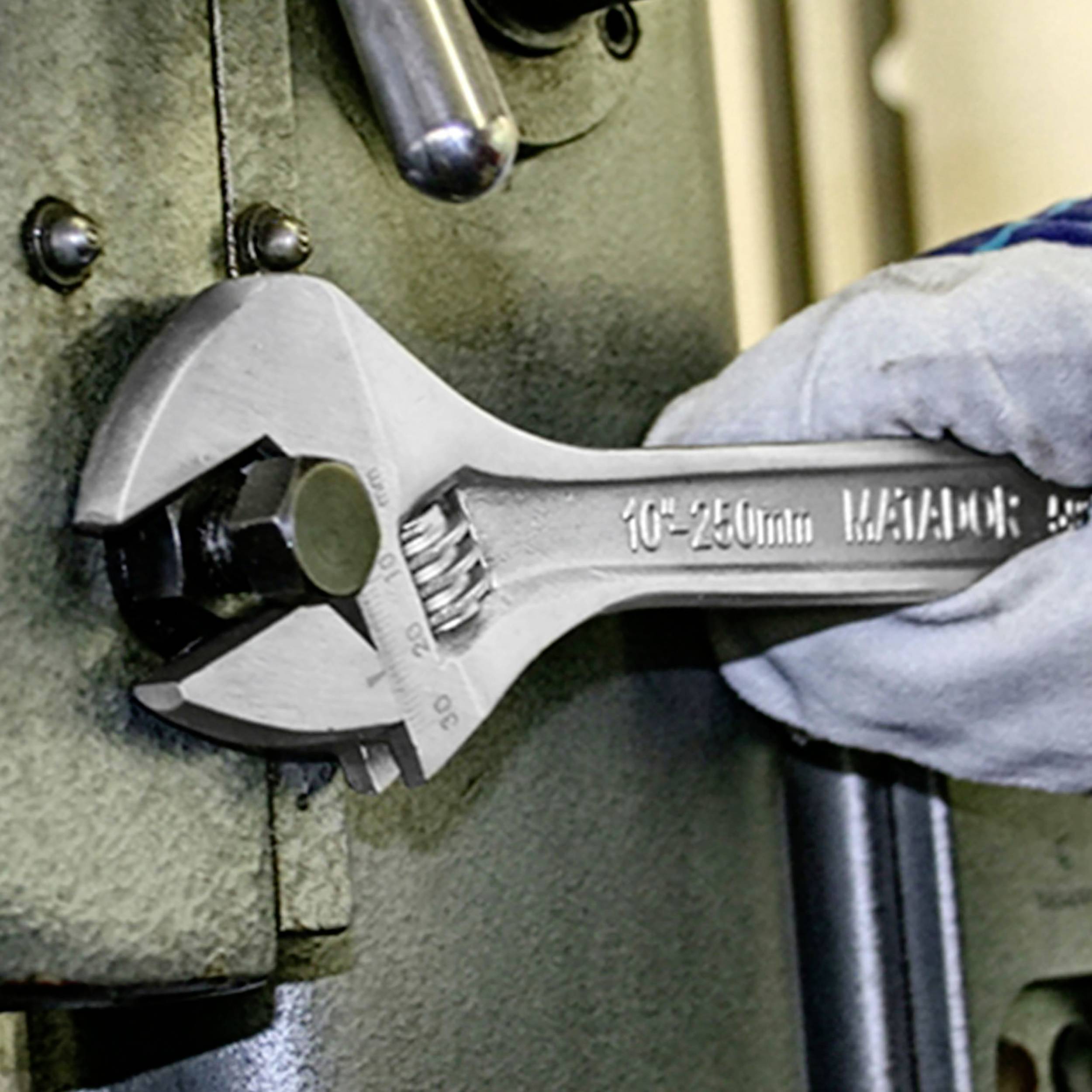 Een hand houdt een verstelbare moersleutel vast die werkt aan een metalen constructie. De moersleutel toont de afmetingen '10"-250mm'.