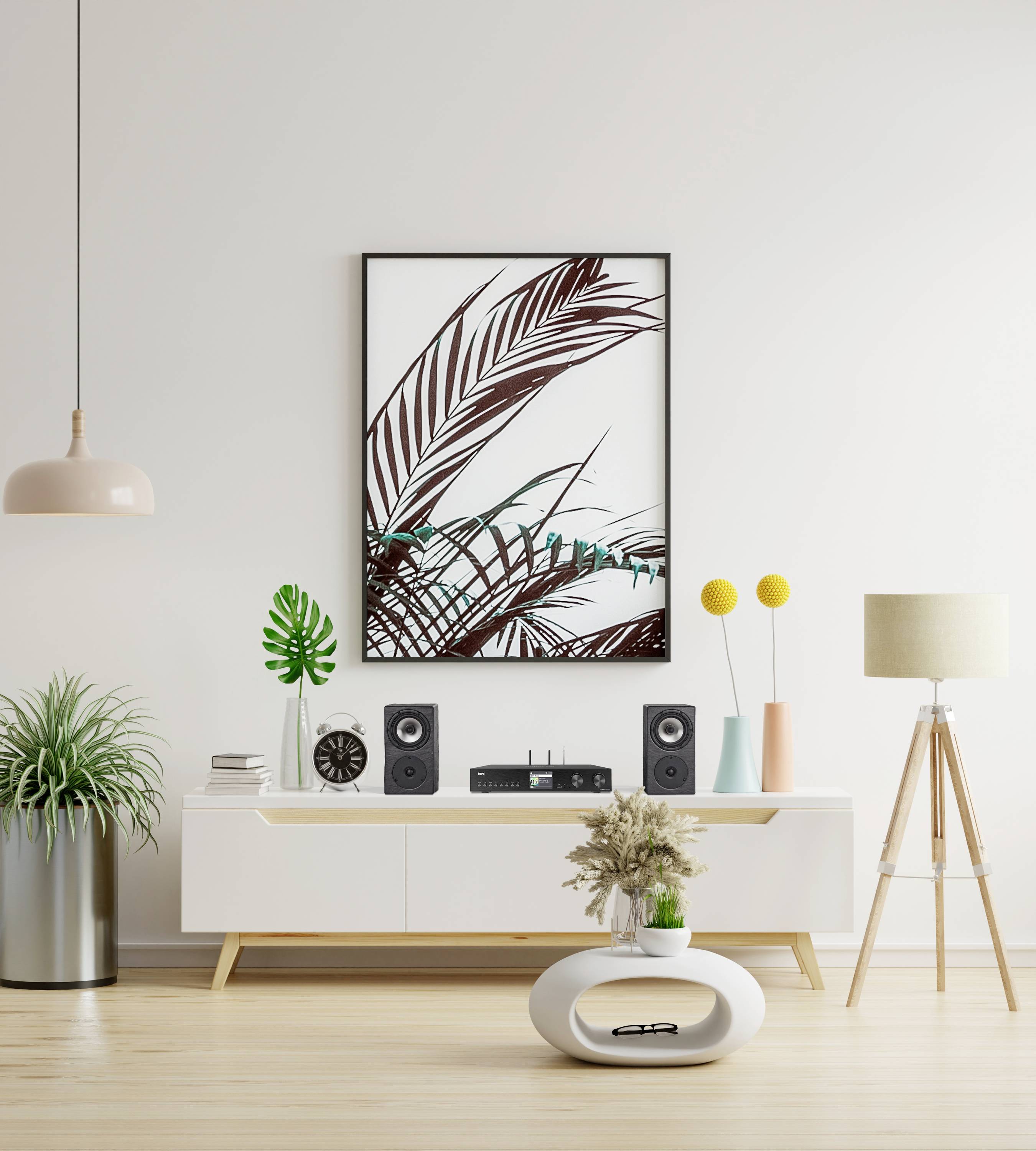 Modern woonkamer met minimalistische decoratie: Witte ladenkast, planten, speakers en een schilderij met palmenmotief aan de muur.