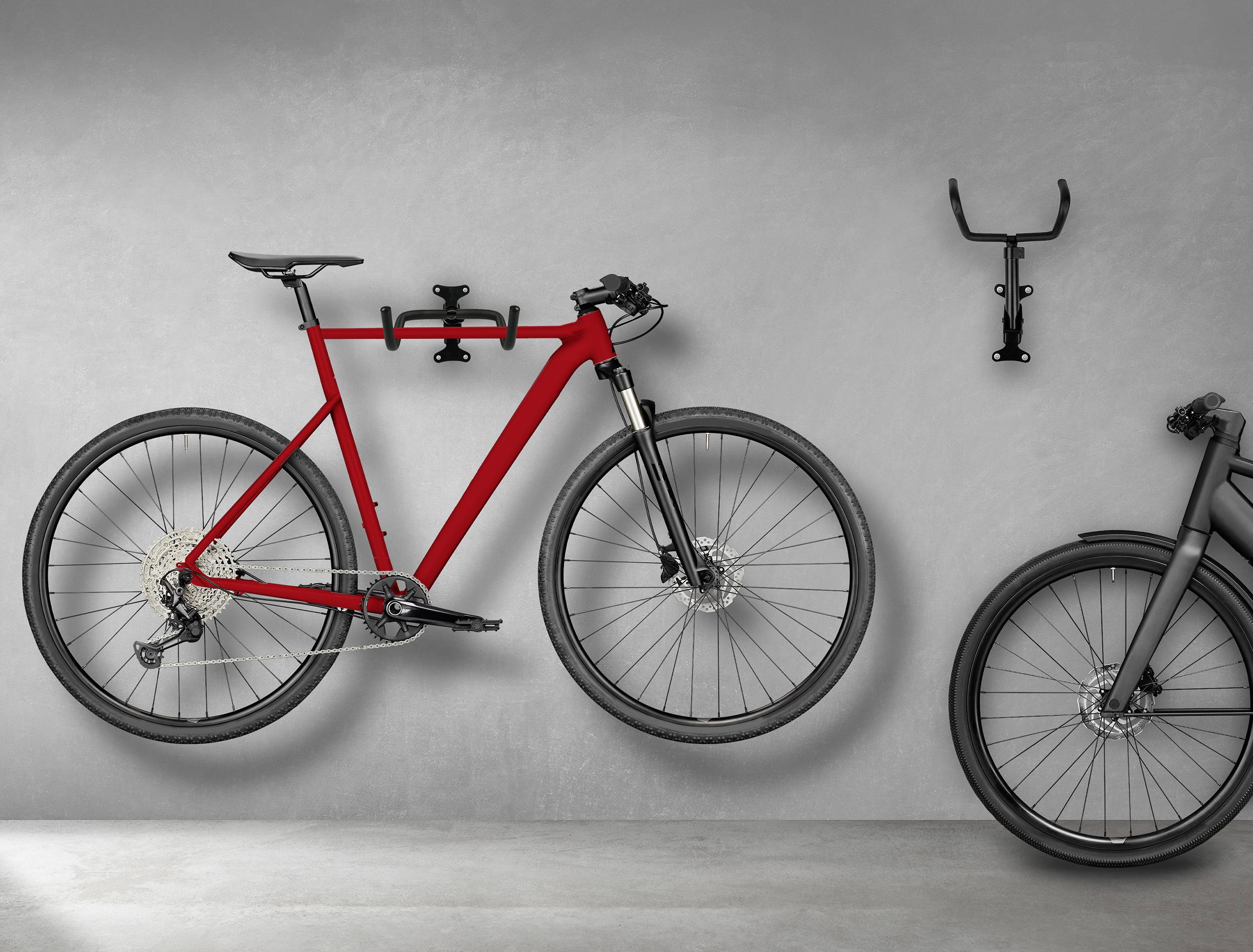 Twee fietsen tegen een betonnen muur, waarvan één rood is en aan een wandsteun hangt, terwijl de andere op de grond staat.