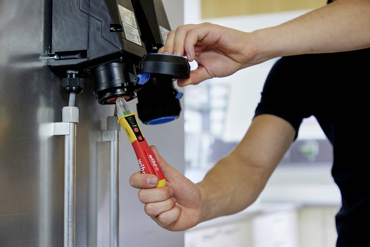 Een persoon gebruikt een meetinstrument voor spanningsmetingen aan een elektrische installatie in een industriële omgeving.