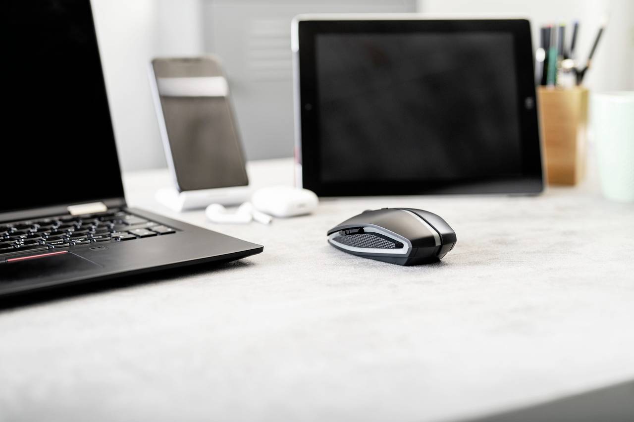 Laptop, muis, tablet en smartphone op een bureau. Apparaten zijn uitgeschakeld. Kantooromgeving met bureaubenodigdheden op de achtergrond.