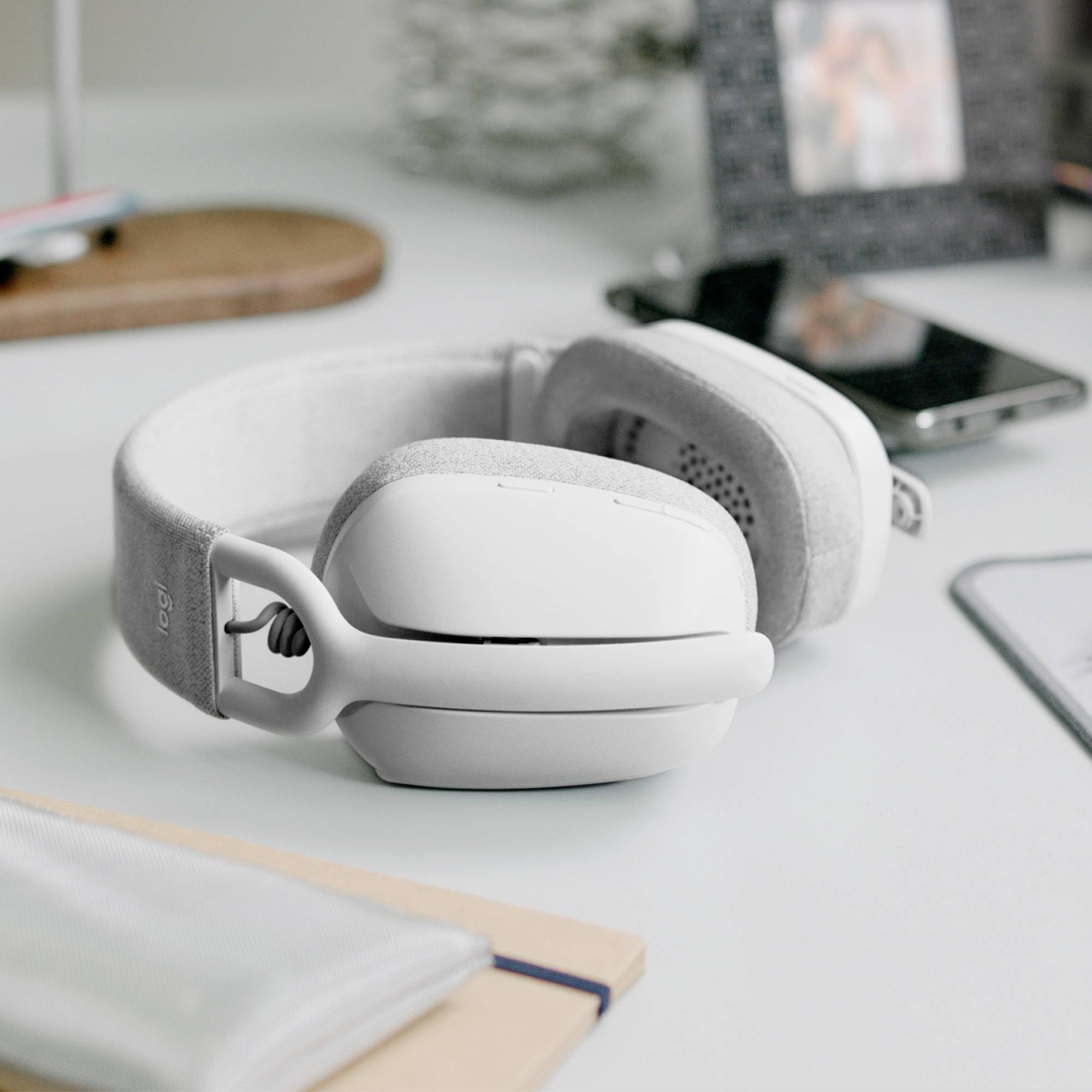 Witte over-ear koptelefoon ligt op een bureau, omringd door onscherpe objecten zoals een lijst en boeken.