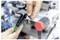 Een persoon gebruikt een handheld gereedschap op een stuk stof in een industriële omgeving, met focus op gedetailleerd werk.