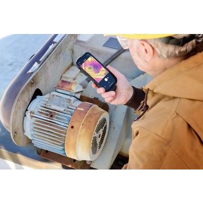 Een persoon met een gele veiligheidshelm inspecteert een motor en gebruikt een smartphone met warmtebeeldcamera om de temperatuur te controleren.
