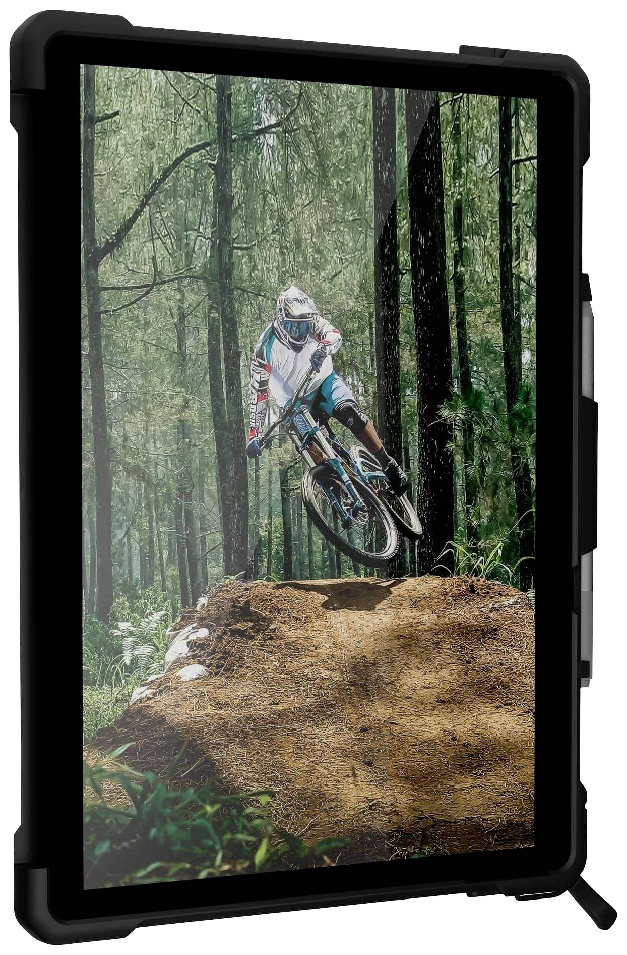 Een mountainbiker springt met zijn fiets over een aarden heuvel in het bos. Omringd door hoge bomen en dicht groen.